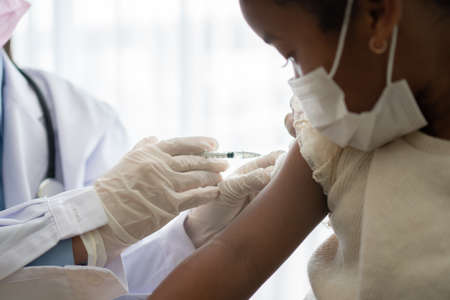Asian doctor user syringe needle for injection vaccinate,  African American children are being  vaccinated for prevention  and flu. Concept of immunization from inoculationの写真素材