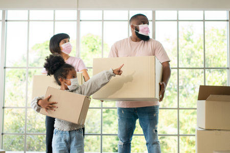 Mixed Race families are carrying cardboard boxes and walking from the front door into the house in a...