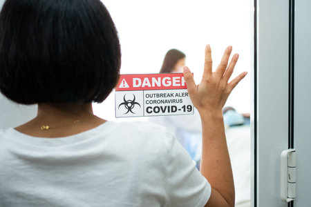 A Wife standing in front of the Quarantine room And put a hand on the mirror While waiting for the...