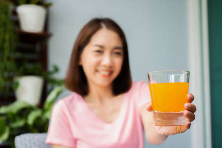 Mid-age Asian woman reading a book and hold orange juice glass in the home. Concept of  Health care And eating for healthyの写真素材