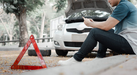 Asian man using smartphone for assistance after a car breakdown on street. Concept of vehicle engine...