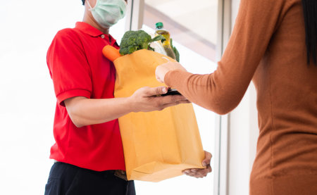 Asian delivery man holding holding a bag of fresh food for giving to customers and holding...