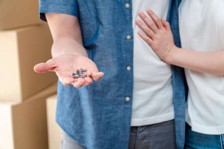 Happy smiling couple in front of the home and holding keys to New Home On Moving In Day, and start a new life family. Concept of homeowner and relocationの写真素材