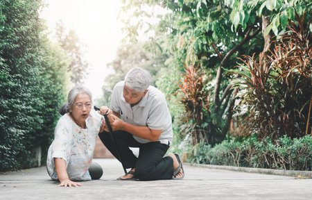 Asian senior woman falling down on lying floor at home after Stumbled at the doorstep and Crying in pain and her husband came to help support. Concept of old elderly insurance and health careの写真素材