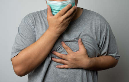 Sick Asian man wearing a medical face mask and Coughing and covering his mouth with my hand. Concept of protection pandemic coronavirus and respiratory diseaseの写真素材