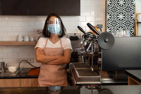 Portrait of a happy woman Asian waitress wearing a face mask and  standing at a coffee shop, Small business owner and startup with a cafe shop conceptの写真素材