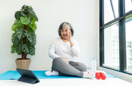 Senior Asian woman watching online courses on a laptop while exercising in the living room at home. Concept of workout training online.の写真素材