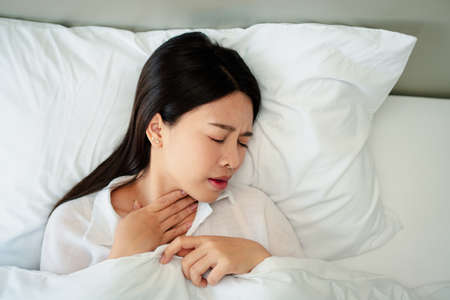Unhappy exhausted woman closed eyes lying in bed cause of Headache, sore throat and tired, Concept of recuperation from illness, feeling unwell and healthcare.の写真素材