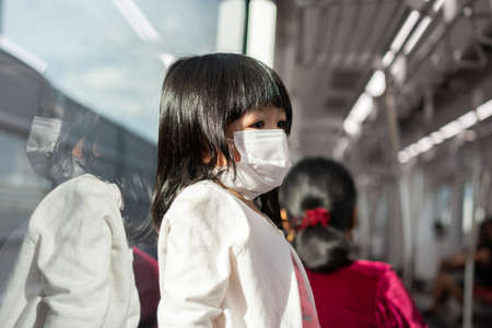 Little girl with surgical mask face protection flu and Virus outbreak in public transportation (skytrain or subway). Concept of New normal lifestyle, Using public transport to travel to school.の写真素材