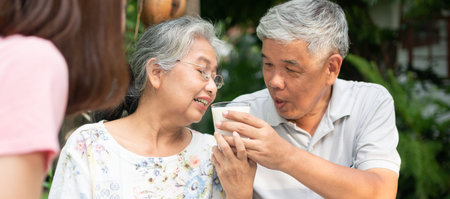 Happy Asian family enjoy lunch together in backyard. Husband feeding milk wife. Concept of a happy...