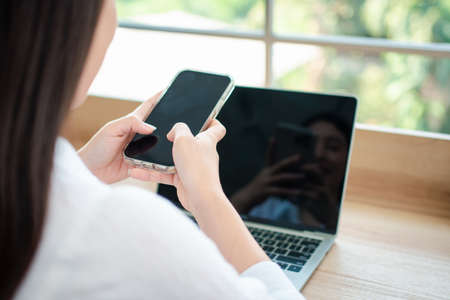 Happy beautiful asian woman working on a laptop and smartphone at the home office sitting at table. Happy female professional freelancer online using notebook pc and smartphone concept.の写真素材