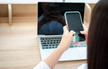 Happy beautiful asian woman working on a laptop and smartphone at the home office sitting at table. Happy female professional freelancer online using notebook pc and smartphone concept.の写真素材