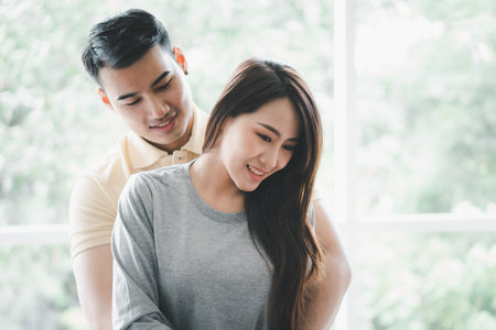 Happy couple sitting on the sofa and being a man teases his girlfriend with love in the living room and relax. Concept of romantic on valentine day. Proposal and marriageの写真素材