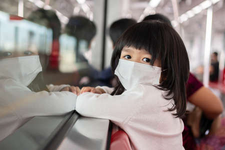 Little girl with surgical mask face protection flu and Virus outbreak in public transportation (skytrain or subway). Concept of New normal lifestyle, Using public transport to travel to school.の写真素材