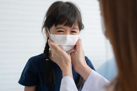 Asian parents wear face masks to little daughter for protection  before going to school. Mom teaches daughter to put on a medical maskの写真素材