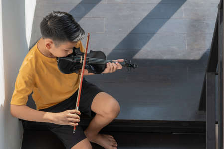 A Little Asian kid playing and practice violin musical string instrument against in home, Concept of Musical education, Inspiration, Teenager art school student.の写真素材