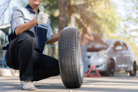 Expertise mechanic man in uniform holding a tire for help a woman for changing car wheel on the...