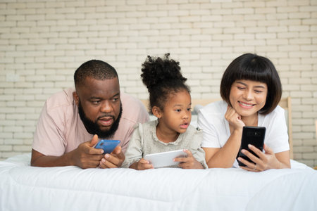 The family has fun and plays education games online with a smartphone at home in the bedroom....