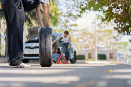 Expertise mechanic man in uniform holding a tire for help a woman for changing car wheel on the highway, car service, repair, maintenance concept.の写真素材