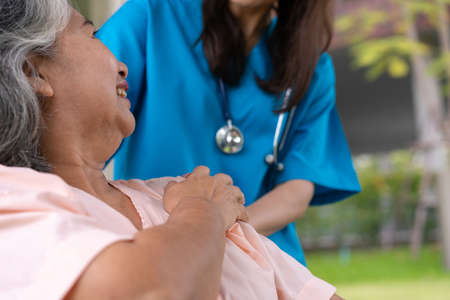 Asian careful caregiver or nurse hold the patient hand and encourage the patient in a wheelchair.  Concept of happy retirement with care from a caregiver and Savings and senior health insurance.の写真素材