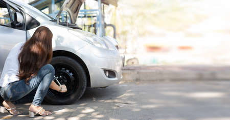Smart and Attractive Asian woman jacks up her car and uses a wrench to change the wheel on a broken car, uses tools or equipment, tries to solve problems by self, Car Repairing and insurance conceptの写真素材