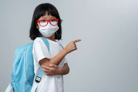 Portrait of Asian girl kid with protective face mask with school backpack and point the finger. Concept of kid going back to school and new normal lifestyleの写真素材