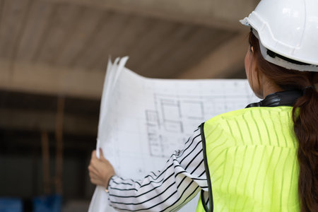 Asian engineer or Young woman Architect put on a helmet for safety and look at Blueprint for Inspect...
