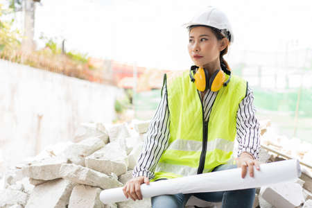 Asian engineer or Young woman Architect put on a helmet for safety and look at Blueprint for Inspect Building factory Construction Site on a construction site. Smart working woman concept.の写真素材