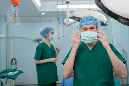 Portrait of Asian surgeon with medical mask standing in operation theater at a hospital. Team of...