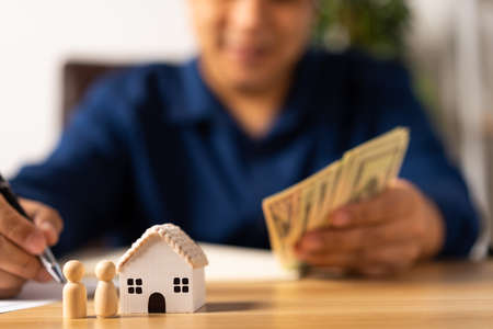 Selective focus for House model and figures people in front Happy Asian man holding a banknote and do financial accounting, Concept for financial planning, mortgage estate, Insurance, and home loanの写真素材
