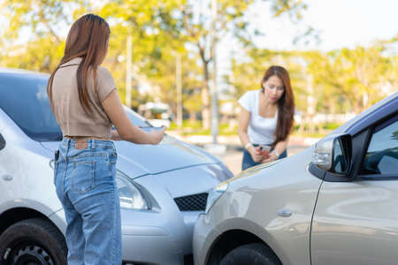 Two drivers check for damage after a car accident before taking pictures and sending insurance. Online car accident insurance claim idea after submitting photos and evidence to an insurance company.の写真素材