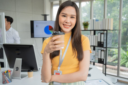 Young Asian Happy Businesswoman or intern holding coffice cup in Modern Office background is...