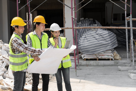 Asian engineer or Young Female Architect put on a helmet for safety and talk with a contractor on a...