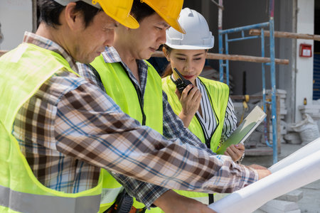 Asian engineer or Young Female Architect put on a helmet for safety and talk with a contractor on a...