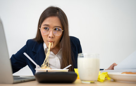 Busy and tired businesswoman eating spaghetti for lunch at the Desk office and working to deliver financial statements to a boss. Overworked and unhealthy for ready meals, burnout concept.の写真素材