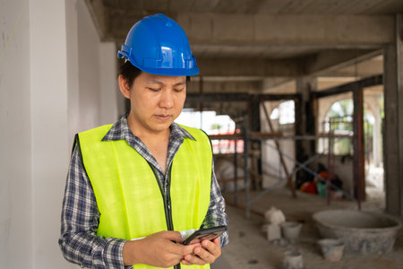 Asian engineer, Young Architect or contractor put on a helmet for safety and use smart phone for take picture and send construction defect to head office. Construction Site and contractorの写真素材