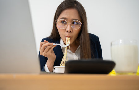Busy and tired businesswoman eating spaghetti for lunch at the Desk office and working to deliver financial statements to a boss. Overworked and unhealthy for ready meals, burnout concept.の写真素材