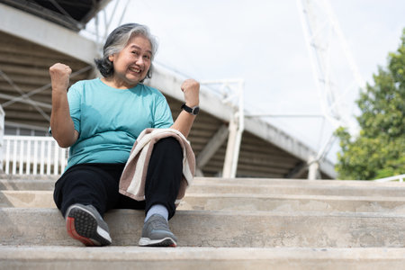 Happy and smile elderly asian woman sitting on stairs for rest after workout, jogging on morning, senior exercise outdoor for good healthy. Concept of healthcare and active lifestyle for healthyの写真素材