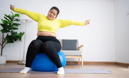 Portrait plus size woman doing exercise with fitness ball in home gym. Overweight woman sitting on a...
