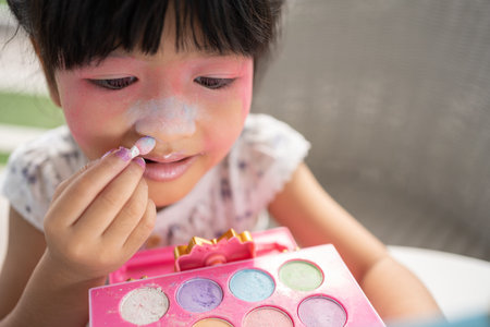 Adorable little child Asian girl paints her mouth with pink children heads and looks in the mirror....