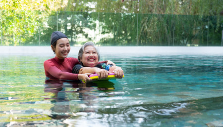 Young trainer helping senior woman in aqua aerobics and working out in the pool. old woman and mature man doing aqua aerobics exercise in swimming pool, Elderly sports, and active lifestyle concept.の写真素材