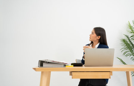 Young pensive businesswoman at desk with laptop dreamful for successful and holding milk glass  isolated on white background.の写真素材