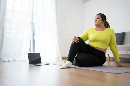 Asian overweight woman doing stretching exercise at home on fitness mat. Home activity training, online fitness class. Stretching training workout on yoga mat at home for good health and body shape.の写真素材