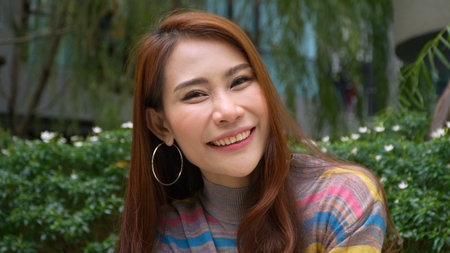 Portrait of a Beautiful Young Woman with Red Hair Wearing colorful Sweater in the garden and Looking Up to the Camera and Smiling, Feel happy. Summer. Outdoors. Slow motionの写真素材