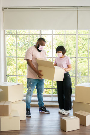 Mixed Race couple American African and Asian a surgical mask is carrying cardboard boxes in a new...