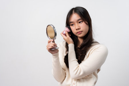 Beautiful young woman makes blush on her face using makeup brush on isolated white background. Teenage girl doing her own makeup. Close up portrait. Copy, empty space for textの写真素材