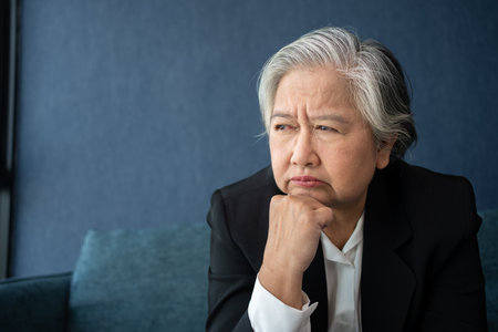 Overworked tired old lady holding head feeling headache. Asian senior business woman stress from hard work. Frustrated business woman thinks seated at workplace, feel distressed looks helpless conceptの写真素材