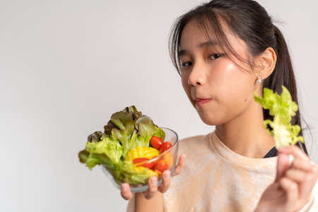 Portrait of a happy playful Asian girl eating fresh salad from a glass bowl after workout at home. Young lady Enjoying Healthy Nutrition And Organic Food, Having Vegetarian Mealの写真素材