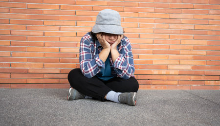 Poor tired stressed depressed elderly Asian woman homeless sitting on the street in the shadow of the building and begging for help and money, Elderly Asian woman abandoned conceptの写真素材