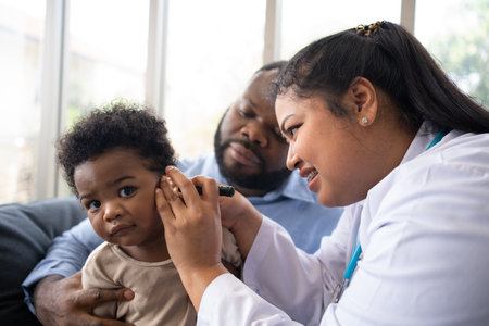 Pediatric doctor examining ear for a hearing test examining cute little girl in medical healthcare hospital or clinic. Smiling African American Baby whit pediatrician in hospitalの写真素材